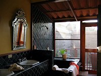The main part of the bathroom has double sinks and a deep bath/shower finished in tile.  The rear of the bathroom is all screens, opening into an outdoor stone courtyard with another shower outside.  